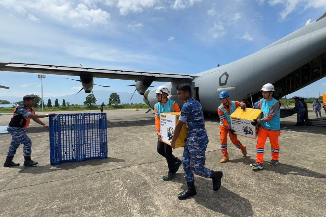 Personel PLN dan TNI Angkatan Udara bergotong royong memindahkan genset dan material tower darurat dari pesawat Hercules